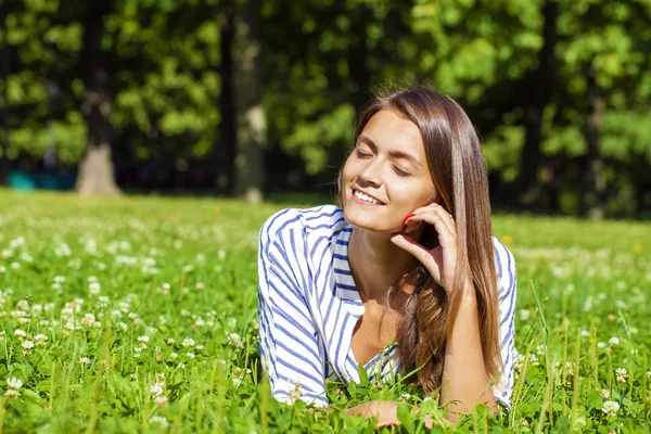 Attractive young brunette woman lying on green grass field at su — Stock Photo, Image