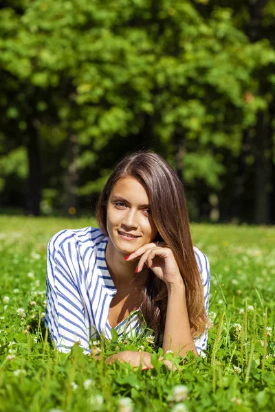 Attractive young brunette woman lying on green grass field at su — Stock Photo, Image