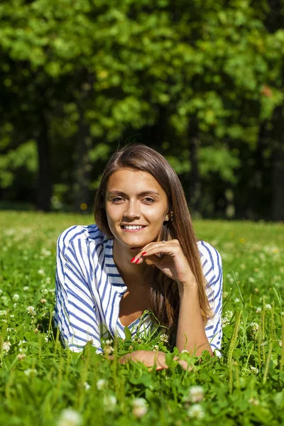 Attraktiv ung brunett kvinna liggande på grönt gräs fält på su — Stockfoto