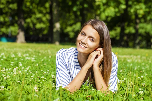 Attractive young brunette woman lying on green grass field at su — Stock Photo, Image
