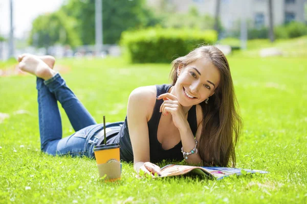 Jonge vrouw lezen tijdschrift liggen op gras — Stockfoto