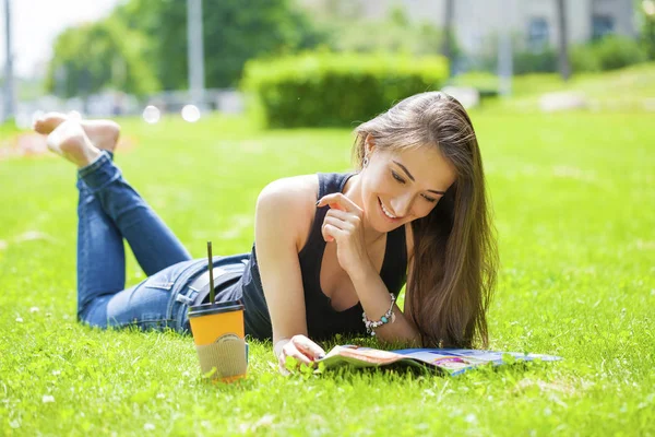 Giovane donna che legge rivista sdraiata sull'erba — Foto Stock