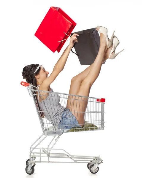 Ung vacker brunett flicka sitter i en tom shopping cart wit — Stockfoto
