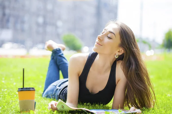 Jovem mulher leitura revista deitado na grama — Fotografia de Stock