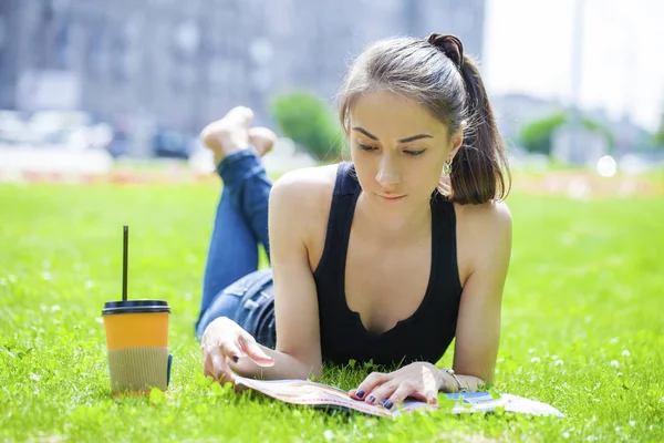 Ung kvinna läser tidningen liggande på gräs — Stockfoto