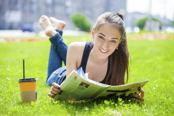 Νεαρή γυναίκα ανάγνωση περιοδικό ξαπλωμένος στο γρασίδι — Φωτογραφία Αρχείου