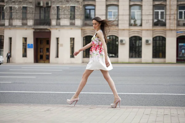 Young beautiful brunette woman in white flowers dress walking on — Stock Photo, Image