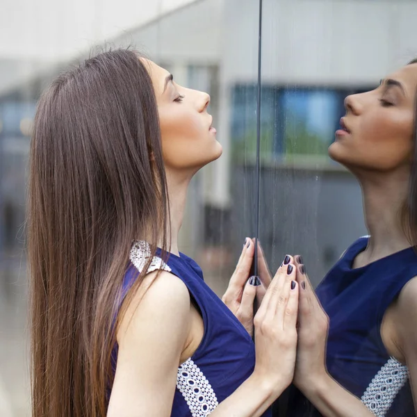 Elegante dama en vestido azul posando cerca de la pared espejada —  Fotos de Stock