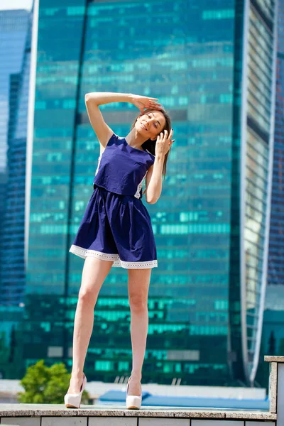 Jovem mulher em um vestido azul está se esticando perto de arranha-céus — Fotografia de Stock