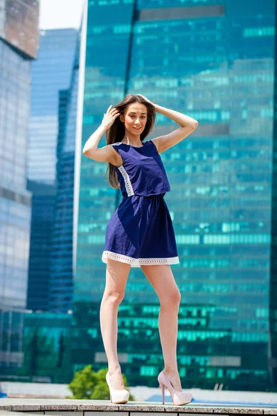 Mladá žena v modrých šatech se protahuje poblíž mrakodrapy — Stock fotografie
