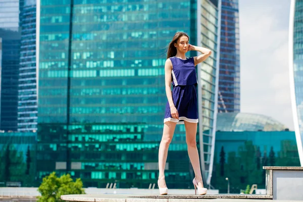 Young woman in a blue dress is stretching near skyscrapers — Stock Photo, Image