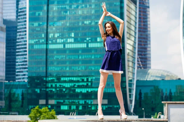 Young woman in a blue dress is stretching near skyscrapers — Stock Photo, Image