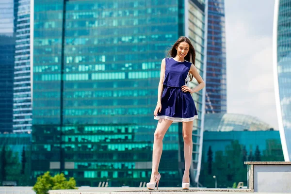 Молодая женщина в синем платье растягивается возле небоскребов — стоковое фото