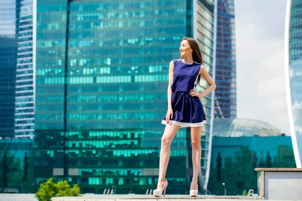 Fiatal nő, egy kék ruhát, nyújtás, felhőkarcoló közelében — Stock Fotó