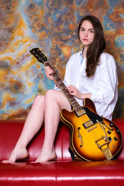 年轻的女孩坐在红色沙发上，与电吉他 — 图库照片
