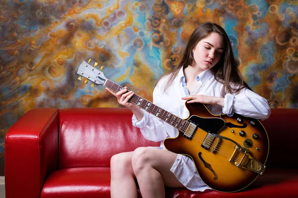Dívka sedící na červené pohovce s elektrickou kytaru — Stock fotografie