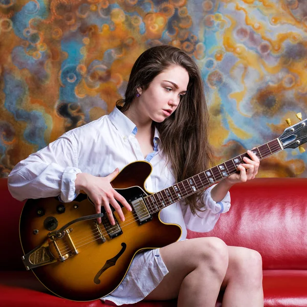 Jovem sentada em um sofá vermelho com guitarra elétrica — Fotografia de Stock