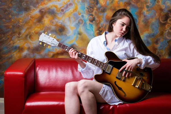 Dívka sedící na červené pohovce s elektrickou kytaru — Stock fotografie