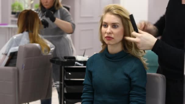 Styling hair in the beauty salon. Young beautiful blonde model in a hairdresser — Stock Video