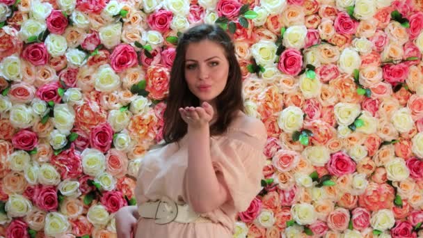Воздушный поцелуй. Портрет молодой сексуальной женщины в розовом платье, на фоне яркой цветочной стены — стоковое видео