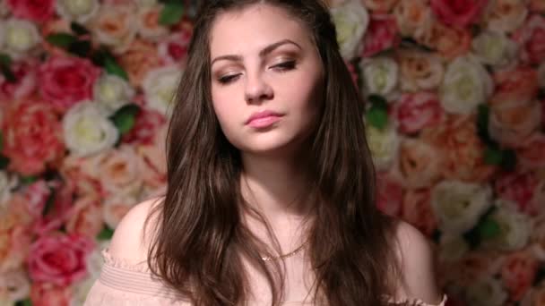 Muotokuva nuori kaunis brunette nainen, lähikuva taustalla kirkas kukka seinä — kuvapankkivideo