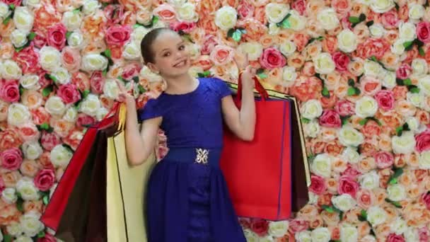 Kindereinkaufen. Porträt eines glücklichen blonden Mädchens in blauem Kleid, Hintergrund einer hellen Blumenwand — Stockvideo