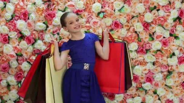 Childrens winkelen. Portret van gelukkig blond meisje in blauwe jurk, achtergrond van de heldere floral wall — Stockvideo