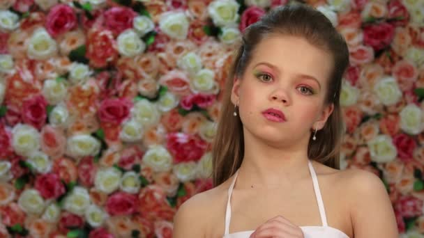 Silencio. Niña en vestido blanco posando sobre un fondo de una pared de flores en el estudio — Vídeo de stock