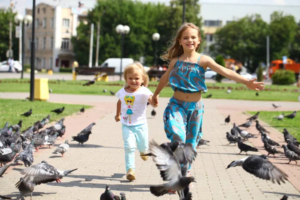 Young happy girl runs through a flock of pigeons on the square — Stock Photo, Image