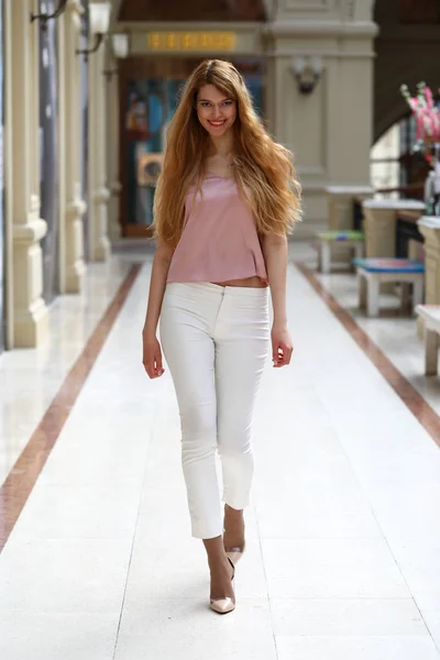 白のパンツとピンクのブラウスで若い美しいブロンドの女性 — ストック写真