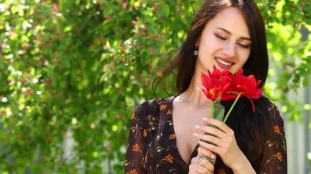 Цветущие тюльпаны. Улыбающаяся брюнетка с красными тюльпанами, весна на открытом воздухе — стоковое видео