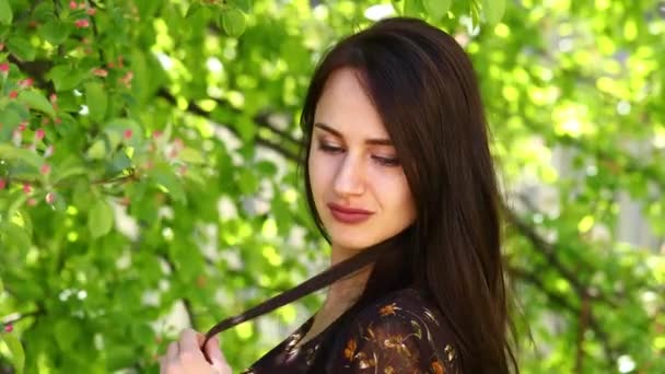 Acalma-te, Brunette. Jovem mulher bonita em um vestido de verão posando contra o parque da primavera ao ar livre — Vídeo de Stock