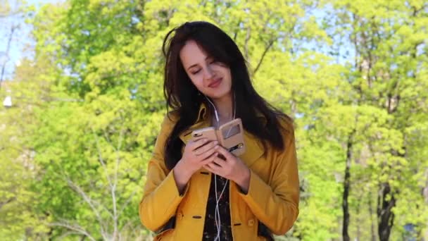 音楽は常に私と一緒にです。若い美しいブルネット女性春公園で歌を聴いて — ストック動画