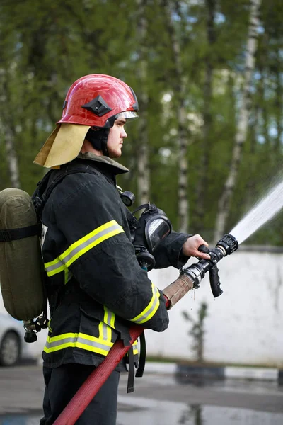 Fireman in fire fighting suit spraying water to fire surround — Stock Photo, Image