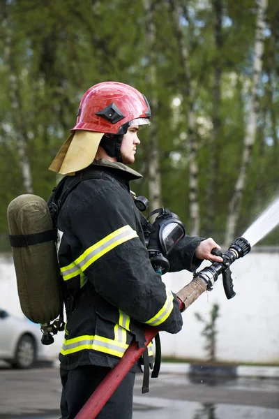 Bombero en traje de extinción de incendios rociando agua para fuego rodear —  Fotos de Stock