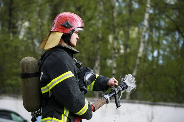 Пожежний у пожежному костюмі обприскує воду до вогню — стокове фото