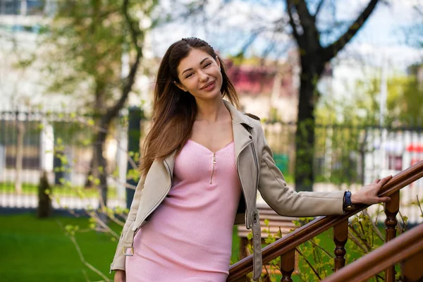 Mooie jonge brunette vrouw in roze jurk en grijze jas — Stockfoto