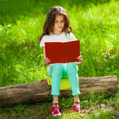 Orman ağaç kütüğü üzerinde oturup kitap ile sevimli küçük kız