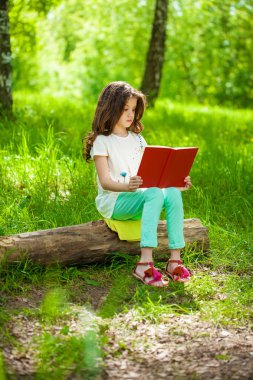 Orman ağaç kütüğü üzerinde oturup kitap ile sevimli küçük kız