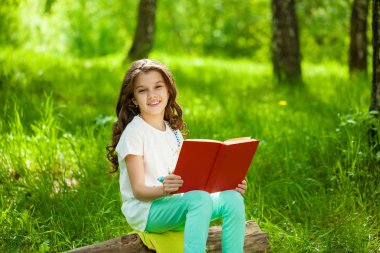 Orman ağaç kütüğü üzerinde oturup kitap ile sevimli küçük kız