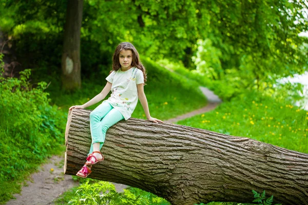 Liten flicka i vit klänning sitter på trädstam över gröna gras — Stockfoto