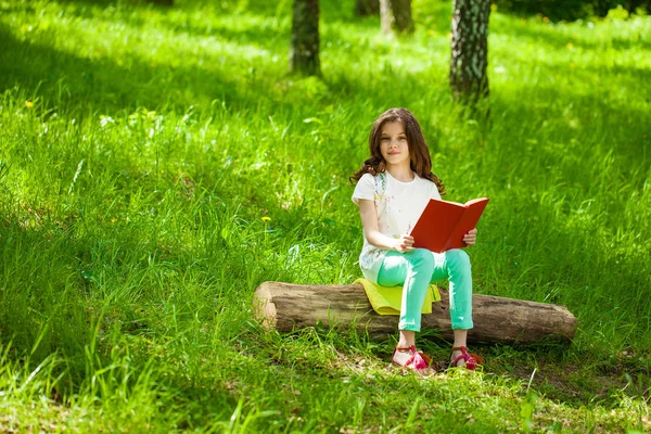 Charming little girl in forest with book sitting on tree stump — Stock Photo, Image