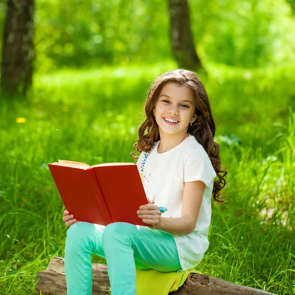 Encantadora niña en el bosque con libro sentado en el tocón del árbol —  Fotos de Stock