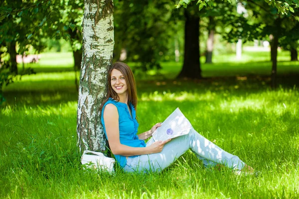 Mulher morena feliz lendo uma revista de mulheres sentada no gr — Fotografia de Stock