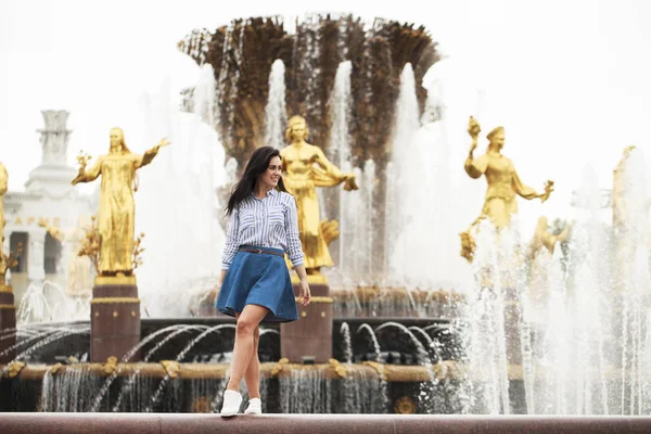 Young beautiful brunette girl posing near city fountain — Stock Photo, Image