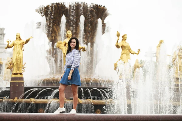 Young beautiful brunette girl posing near city fountain — Stock Photo, Image