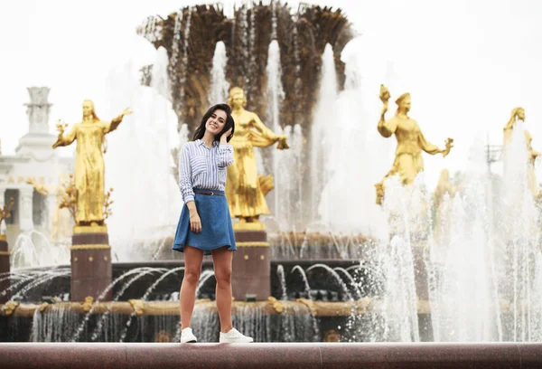 Young beautiful brunette girl posing near city fountain — Stock Photo, Image