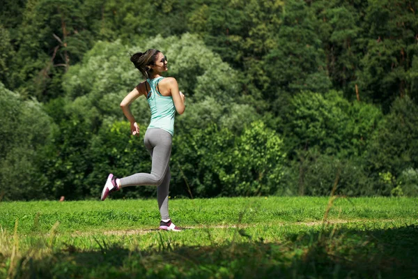 Atletische gelukkig brunette vrouw uit te werken in een weide — Stockfoto