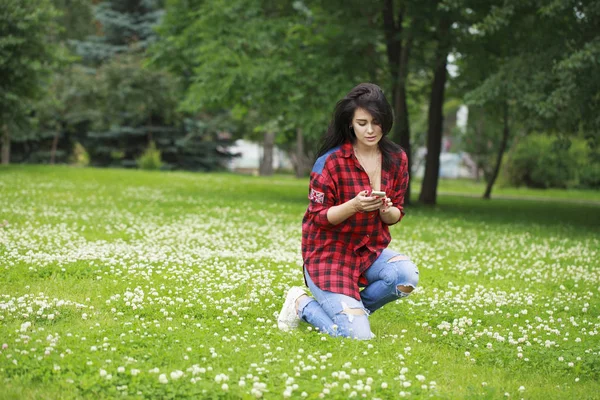 Νεαρή γυναίκα ξαπλωμένη στο γρασίδι διαβάζετε ένα μήνυμα σε ένα κινητό τηλέφωνο — Φωτογραφία Αρχείου