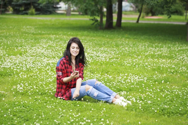Jovem deitada na grama lendo uma mensagem em um telefone celular — Fotografia de Stock